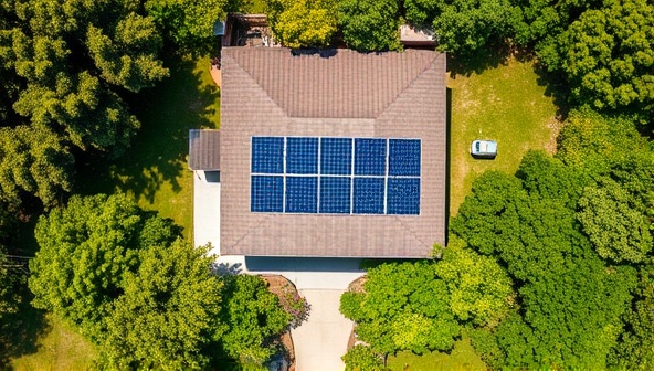 An aerial view of a house with rented solar panels on the roof, surrounded by green trees and a clear blue sky, showcasing a sustainable and eco-friendly lifestyle.