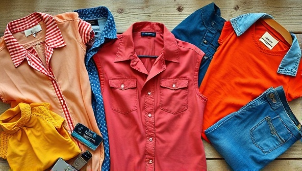 An aesthetically pleasing flat lay of colorful vintage clothing items arranged on a rustic wooden table, with natural lighting highlighting the unique textures and patterns, conveying a sense of style and sustainability.