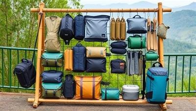 An assortment of neatly organized eco-friendly travel gear items displayed on a sustainable bamboo rack against a backdrop of lush greenery and natural landscapes, showcasing the blend of functionality and environmental responsibility in outdoor exploration.