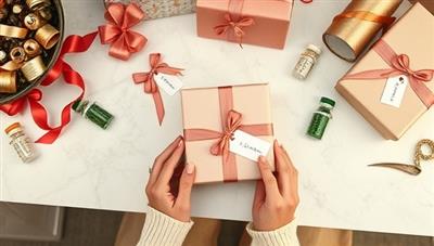 An elegant gift wrapping station with various ribbons, wrapping papers, and personalized gift tags neatly arranged on a chic desk, with hands elegantly wrapping a custom gift box, evoking a sense of luxury and personalization.