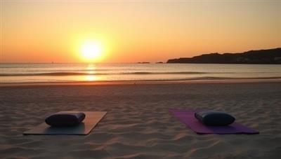 A tranquil beach setting with yoga mats, meditation cushions, and a serene sunset, evoking a sense of relaxation and well-being that embodies the essence of the bespoke wellness retreats offered by the service.