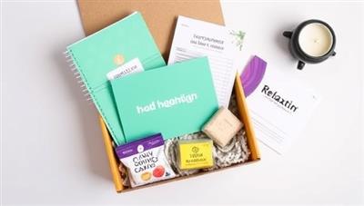 An aesthetically pleasing flat lay image featuring a MoneyMint Box filled with financial wellness goodies, including a budget planner, motivational cards, healthy snacks, and a relaxation candle, creating a sense of wellness and balance in financial management.