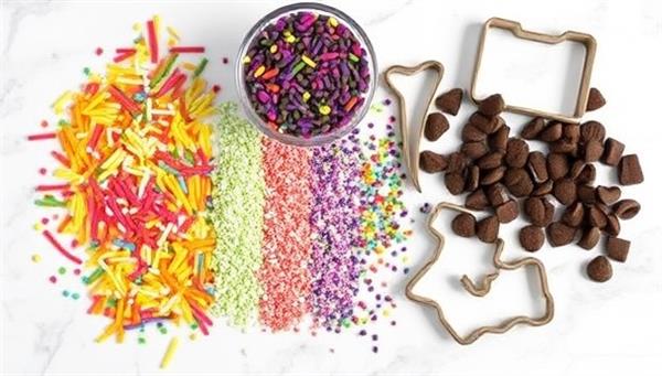 An assortment of colorful sprinkles, chocolate chips, and cookie cutters arranged on a marble countertop, ready to be used in creative dessert-making adventures with Sweet Creations DIY subscription boxes.